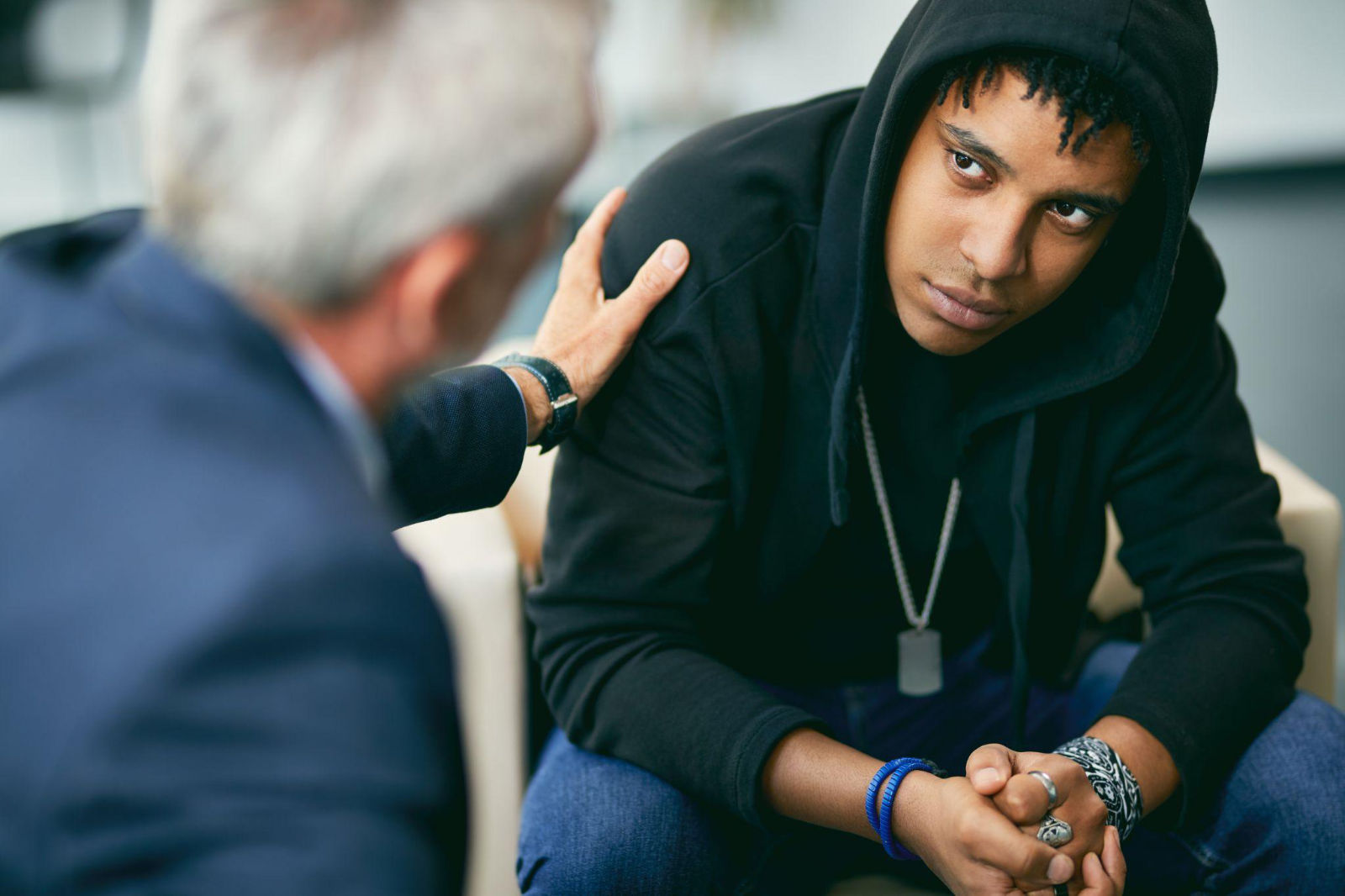 An older man placing a supportive hand on the shoulder of a young man wearing a hoodie during an honest conversation.
