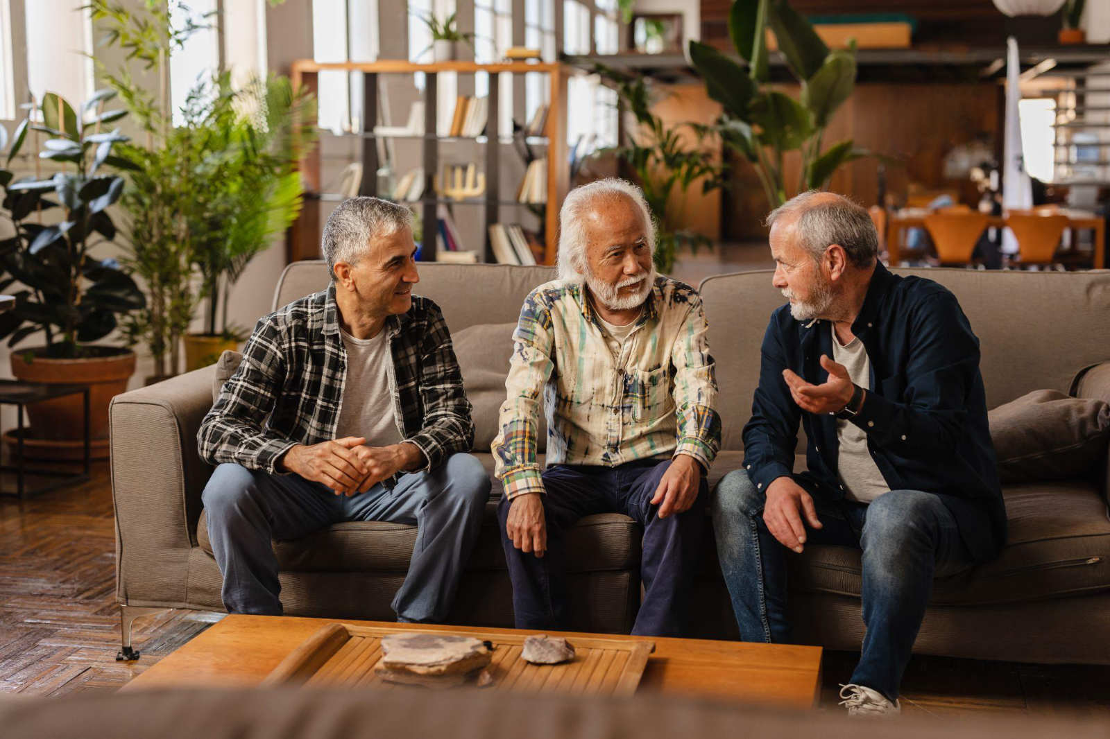 Three men talking comfortably on a sofa in a spacious, warm living environment inside a BC recovery center.