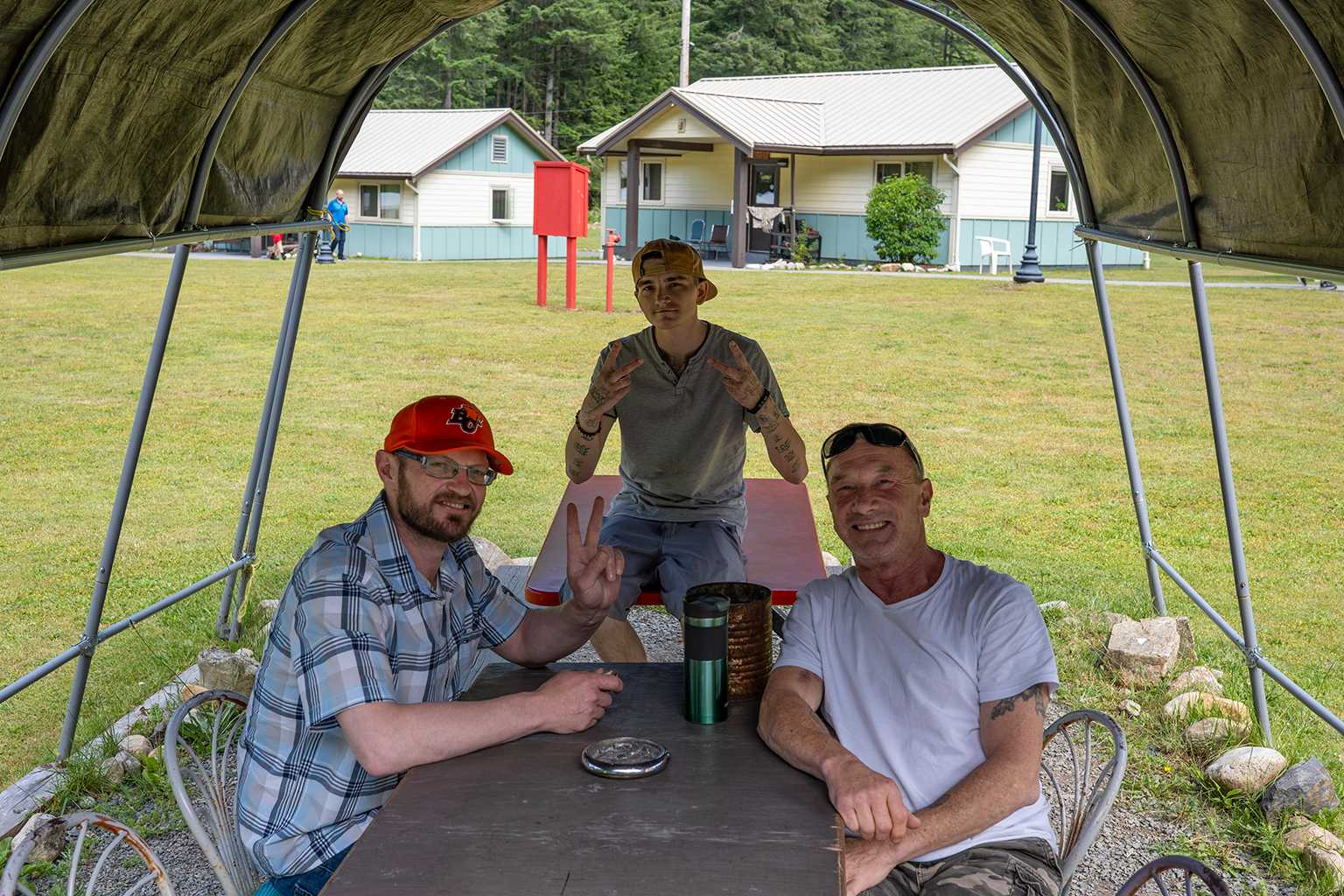 Three men smiling together at an outdoor picnic table outside residential recovery housing at Joshua House.