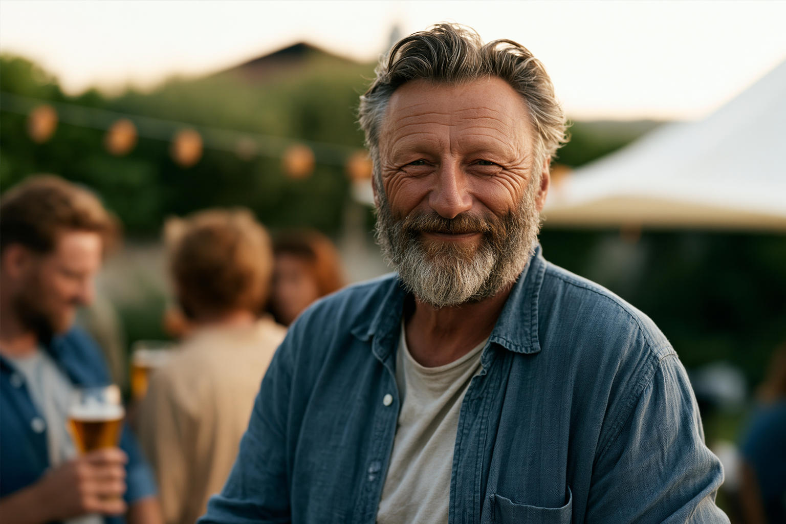 Man smiling outdoors at a social gathering with people drinking beer in the background, illustrating social triggers in recovery.